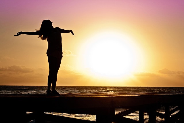 Eine Frau steht bei Sonnenaufgang am Meer - Symbol für Freiheit durch die sanfte Methode vom Yager-Code